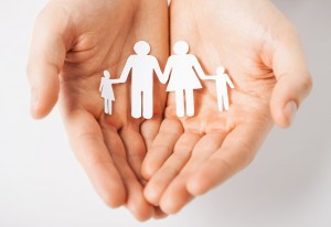 Open hands, offering a folded image in cut paper of a family.